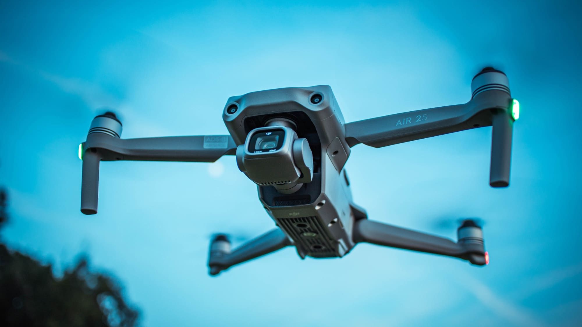 DJI camera drone hovering at dusk with navigation lights on